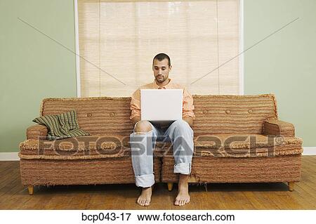 Stock Photo - Man sitting on couch using laptop. Fotosearch