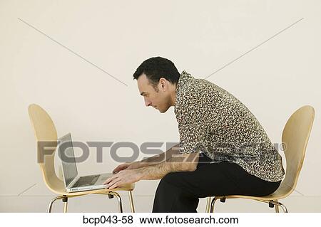 Stock Photo - Man using laptop in bare room. Fotosearch