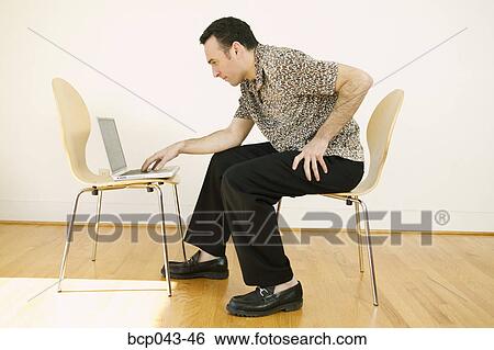 Stock Photograph - Man using laptop in bare room. Fotosearch