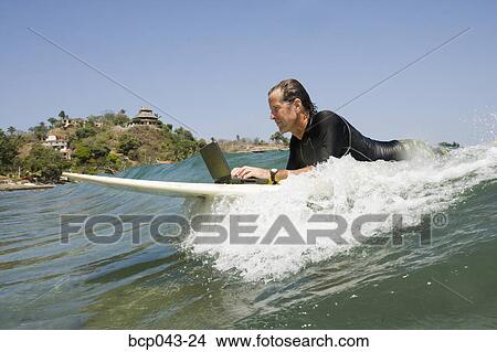 Man using laptop while surfing View Large Photo Image Picture - Man using laptop while surfing. Fotosearch