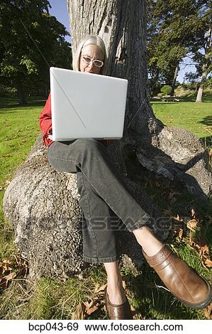 Stock Photo - Woman sitting on tree and using laptop. Fotosearch