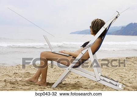 Stock Image - Woman using laptop at beach. Fotosearch
