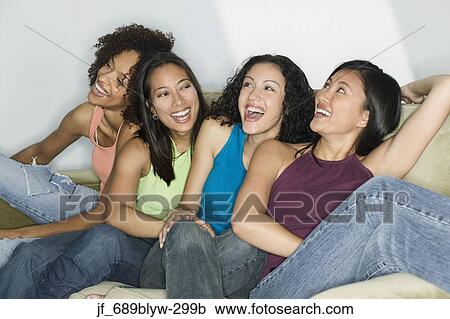 Stock Image - Group of young women sitting on a couch smiling. Fotosearch
