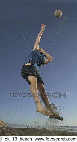 Stock Image - Low angle view of a young man playing volleyball. Fotosearch