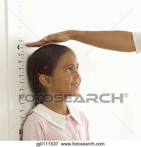 Stock Photo - Person measuring a young girls height against a height chart on the wall. Fotosearch