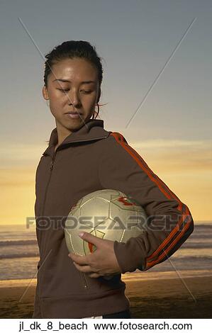 Stock Image - Side profile of a young woman holding a volleyball under her arm. Fotosearch