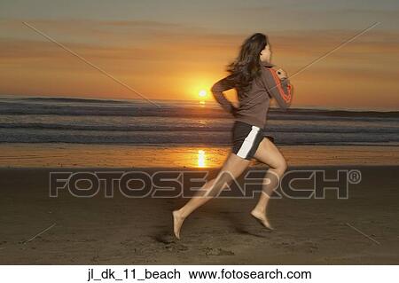 Stock Image - Young woman running at the beach. Fotosearch