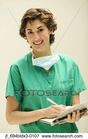 Stock Photo - Female doctor writing in a clipboard looking at camera smiling. Fotosearch
