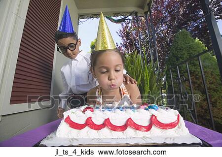 Stock Photograph - Low angle view of a young girl blowing out birthday candles with a young boy standing behind her. Fotosearch