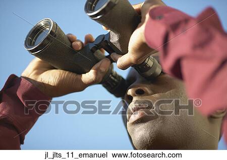 Low angle view of a young man looking through binoculars View Large Photo Image Stock Image - Low angle view of a young man looking through binoculars. Fotosearch