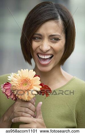 Stock Image - Mid adult woman smiling holding flowers. Fotosearch