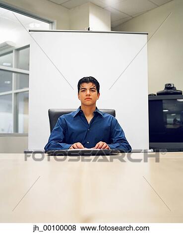 Portrait of a young businessman sitting at a table View Large Photo Image Stock Photo - Portrait of a young businessman sitting at a table. Fotosearch