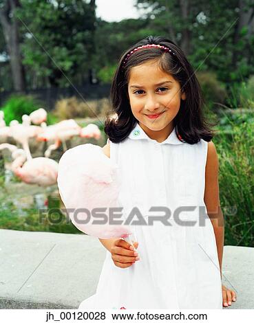 Portrait of a young girl standing holding a stick of cotton candy View Large Photo Image Stock Photo - Portrait of a young girl standing holding a stick of cotton candy. Fotosearch