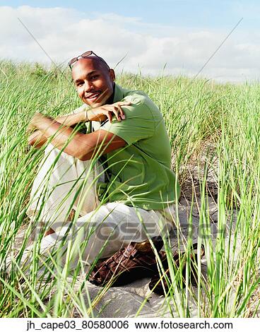 Stock Photograph - Portrait of a young man squatting on a grassy field. Fotosearch