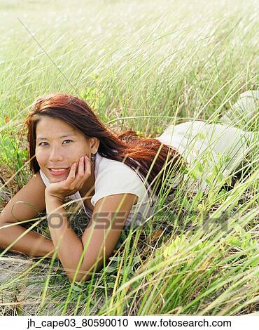 Stock Image - Portrait of a young woman lying in the grass. Fotosearch