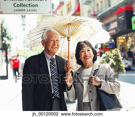 Stock Image - Senior couple standing together holding a parasol. Fotosearch