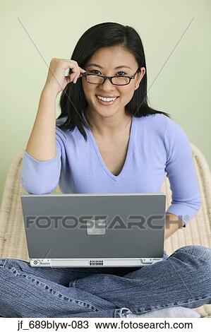 Stock Image - Teenage girl sitting on a bed with a laptop. Fotosearch