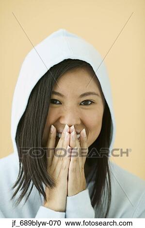 Stock Image - Teenage girl wearing a hooded jacket laughing with her hands on her mouth. Fotosearch