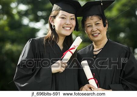 Stock Image - Two female graduates standing together holding diplomas smiling. Fotosearch