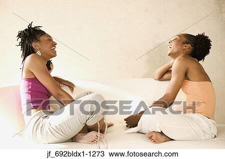 Two young women sitting on a couch laughing View Large Photo Image Stock Image - Two young women sitting on a couch laughing. Fotosearch