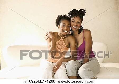Stock Photograph - Two young women sitting on a couch looking at camera smiling. Fotosearch
