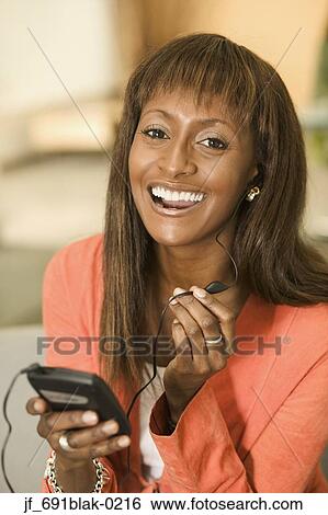 Stock Photograph - Woman holding a mobile phone looking at camera smiling. Fotosearch