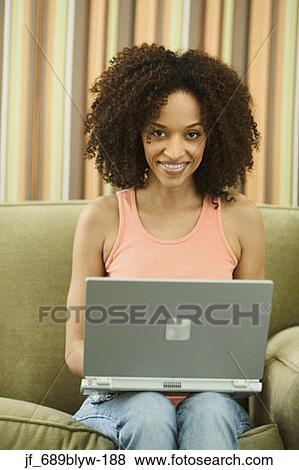 Woman sitting on a couch with a laptop looking at camera View Large Photo Image Stock Photo - Woman sitting on a couch with a laptop looking at camera. Fotosearch