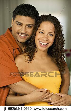 Stock Image - Young couple holding each other smiling looking at camera. Fotosearch