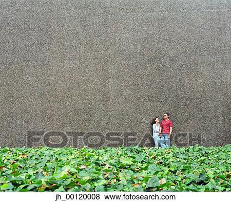 Young couple standing together against a wall View Large Photo Image Stock Photo - Young couple standing together against a wall. Fotosearch