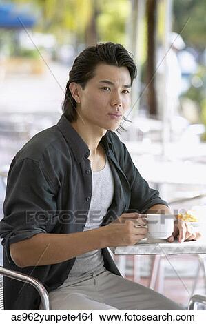 Young man sitting at a table in an outdoor cafe View Large Photo Image Picture - Young man sitting at a table in an outdoor cafe. Fotosearch