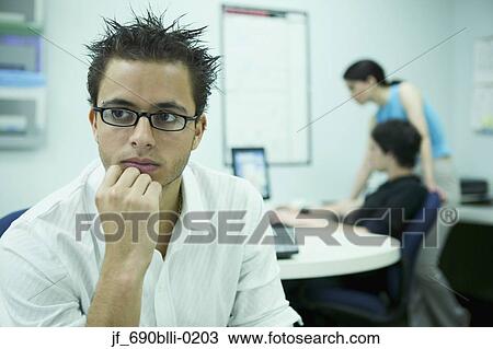 Young man sitting in an office with people working behind View Large Photo Image Stock Image - Young man sitting in an office with people working behind. Fotosearch