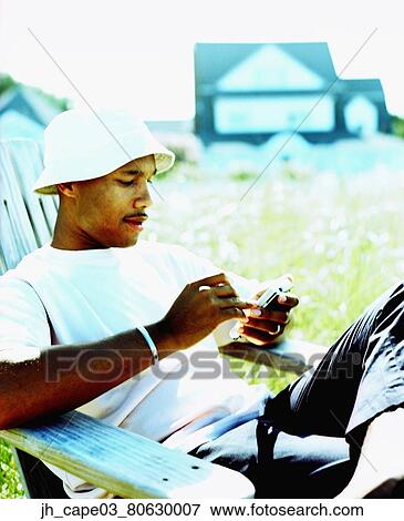 Young man sitting on a chair looking down at a hand held device View Large Photo Image Stock Photo - Young man sitting on a chair looking down at a hand held device. Fotosearch