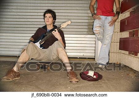 Young man sitting on a skateboard playing a guitar View Large Photo Image Picture - Young man sitting on a skateboard playing a guitar. Fotosearch