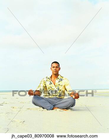 Young man sitting on sand meditating View Large Photo Image Stock Photo - Young man sitting on sand meditating. Fotosearch