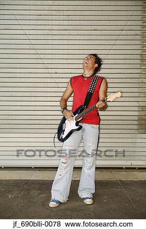 Young man standing playing a guitar View Large Photo Image Stock Photo - Young man standing playing a guitar. Fotosearch