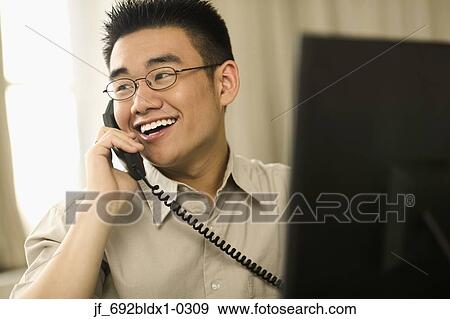 Young man talking on a phone smiling View Large Photo Image Stock Photo - Young man talking on a phone smiling. Fotosearch