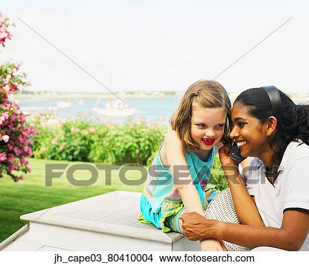 Young woman and a young girl listening on a phone View Large Photo Image Picture - Young woman and a young girl listening on a phone. Fotosearch