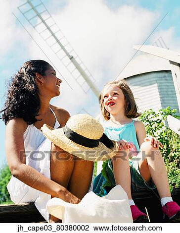 Stock Image - Young woman and a young girl sitting together on a step talking. Fotosearch