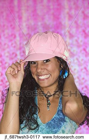 Stock Photo - Young woman holding a cap on her had looking at camera smiling. Fotosearch