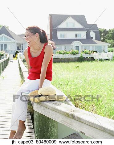 Young woman sitting on a railing smiling View Large Photo Image Stock Photo - Young woman sitting on a railing smiling. Fotosearch