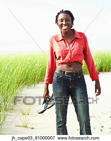 Stock Photo - Young woman standing on a trail holding her sandals. Fotosearch