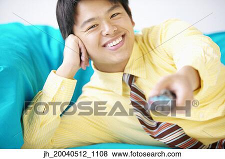 Businessman lying on a couch operating a remote control View Large Photo Image Stock Photo - Businessman lying on a couch operating a remote control. Fotosearch