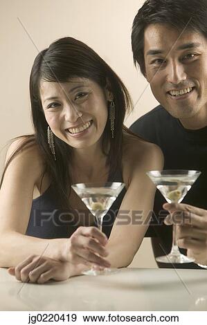 Stock Photo - Couple holding martini glasses looking at camera. Fotosearch