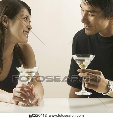 Stock Image - Couple sitting together holding martini glasses. Fotosearch