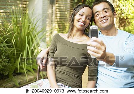 Couple sitting together looking at a mobile phone View Large Photo Image Stock Image - Couple sitting together looking at a mobile phone. Fotosearch