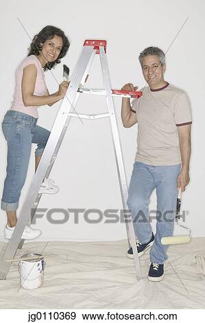 Couple standing on a ladder painting a wall View Large Photo Image Stock Photo - Couple standing on a ladder painting a wall. Fotosearch