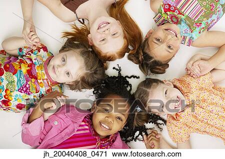 Stock Image - High angle view of a group of young girls lying down together smiling. Fotosearch