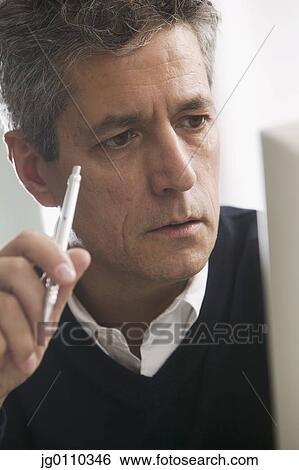 Man holding a pen looking at a computer screen View Large Photo Image Stock Photograph - Man holding a pen looking at a computer screen. Fotosearch