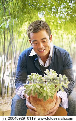 Stock Photo - Mid adult man sitting holding a potted plant. Fotosearch
