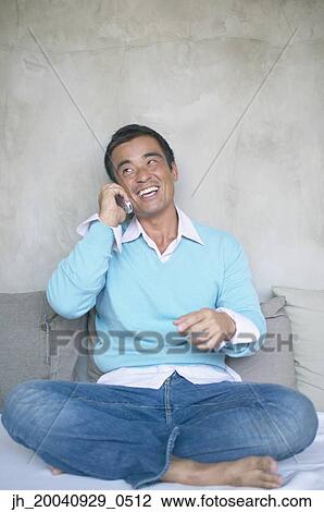 Mid adult man sitting on a be talking on a mobile phone View Large Photo Image Stock Image - Mid adult man sitting on a be talking on a mobile phone. Fotosearch